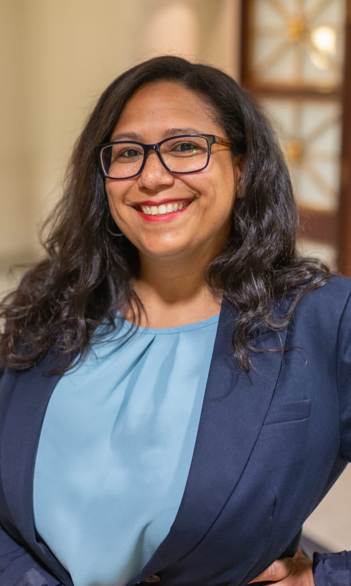 Lesha Sanders smiling in a navy blazer, dark glasses, and blue shirt.